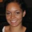 Headshot of a person with a friendly smile, wearing a black top and a white undershirt, against a dark background.