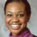 Headshot of a person smiling, wearing hoop earrings and a purple top. The background is plain and neutral.